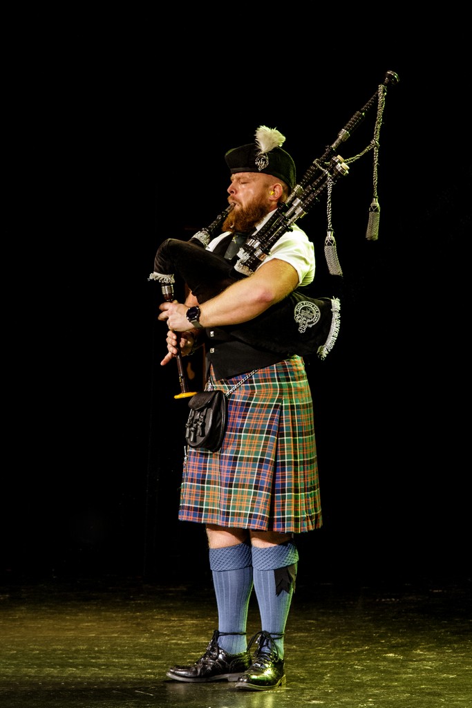 Bagpiper Bruce solo op een groot podium in concertbelichting — Highland Dress en doedelzak